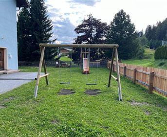 A beautiful playground with a swing and a slide. In the background, there are trees and a meadow.