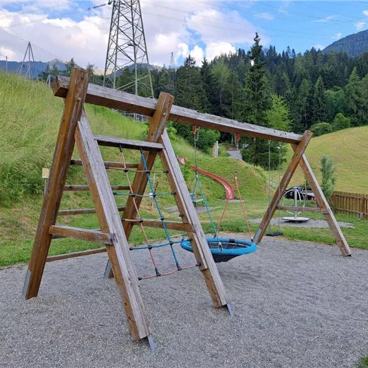 A beautiful playground with a swing and a wooden climbing frame. In the background, green meadows and trees can be seen.