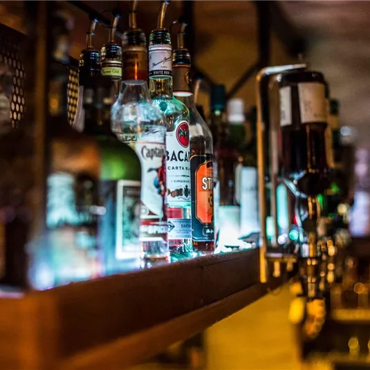 Eine Bar mit einer Auswahl verschiedener Spirituosenflaschen. Die Beleuchtung betont die Gläser und schafft eine einladende Atmosphäre.