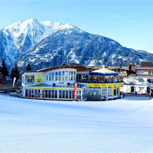 Ein malerisches Skigebiet mit schneebedeckten Pisten und beeindruckenden Bergen im Hintergrund. Die Skihütten sind bunt und einladend, perfekt für eine Pausenversorgung.