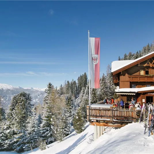 A charming mountain house surrounded by snow-covered trees. Skiers enjoy the sun and the view of the mountains.