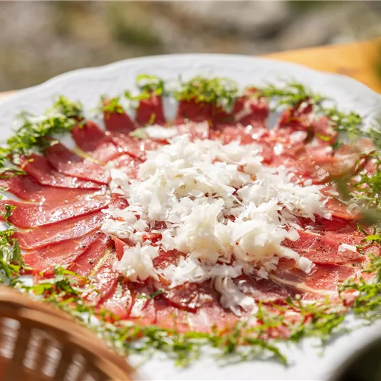 Ein schön angerichteter Teller mit Carpaccio, garniert mit frischem Gemüse und geriebenem Käse. Die Farben und Texturen machen das Gericht appetitlich und einladend.