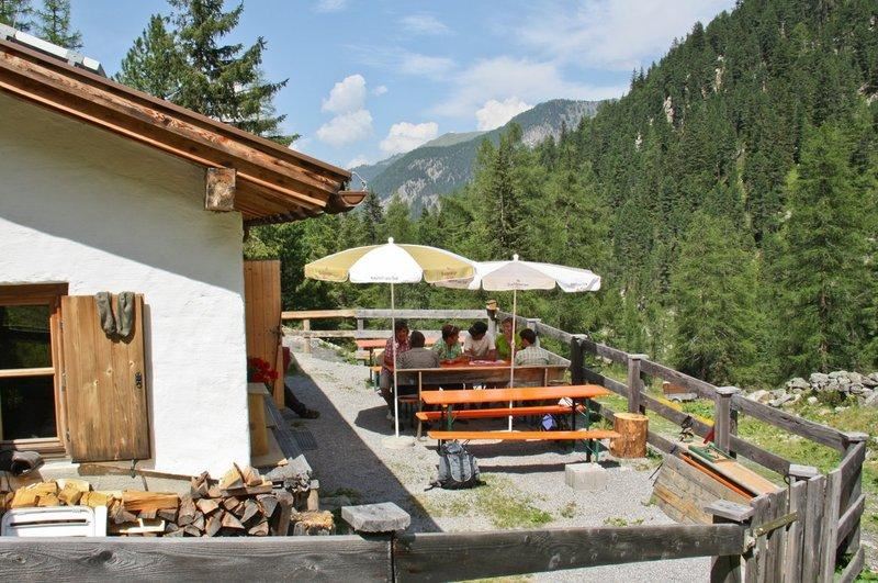 Eine gemütliche Terrasse mit Tischen und Sonnenschirmen inmitten von Bäumen. Im Hintergrund sind die Berge zu sehen.