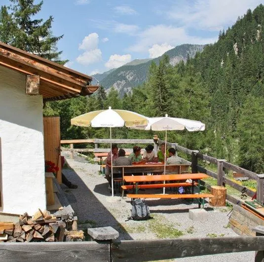 Eine gemütliche Terrasse mit Tischen und Sonnenschirmen inmitten von Bäumen. Im Hintergrund sind die Berge zu sehen.