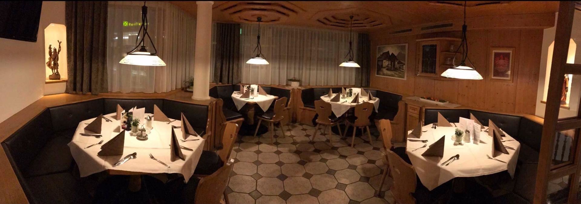 A cozy restaurant with tables set for guests. The warm wood decor and soft lighting create an inviting atmosphere.