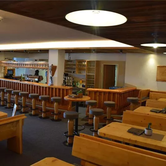 Ein gemütliches Restaurant mit Holztischen und einer langen Bar. Die Beleuchtung schafft eine einladende Atmosphäre.