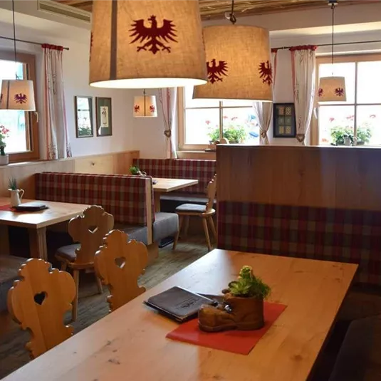 Ein gemütliches Restaurant mit Holzdekor und roten Vorhängen. Die Tische sind mit Pflanzen und Menükarten dekoriert.