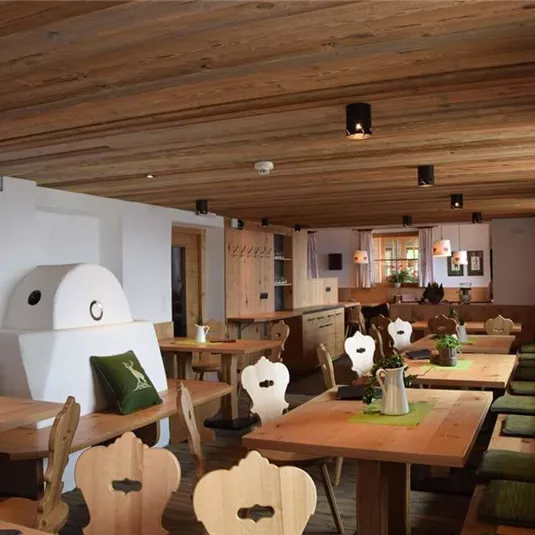 Ein gemütliches Restaurant mit Holzmöbeln und eine warme Atmosphäre. Die Einrichtung ist rustikal mit grünem Dekor und einem großen Holzofen.