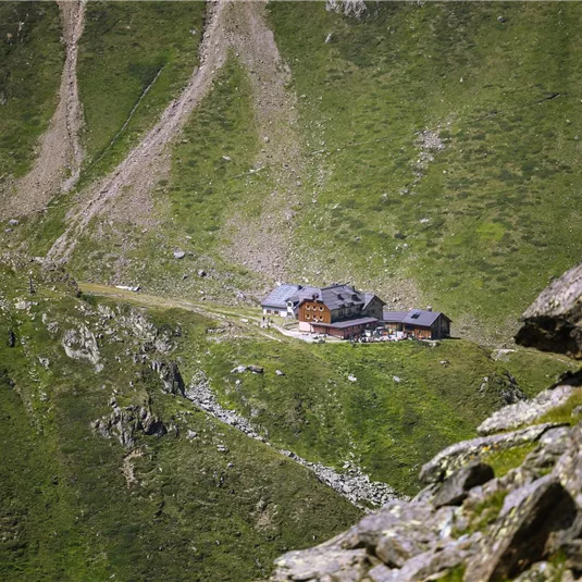 Eine Berglandschaft mit saftigem Grün und steilen Hängen. In der Mitte steht eine kleine Berghütte.