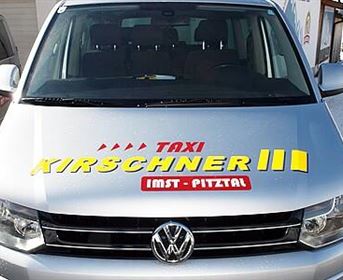 Ein silbernes Taxi mit der Aufschrift "Taxi Kirschner" auf der Frontscheibe. Das Fahrzeug steht in einem schneebedeckten Gebiet.