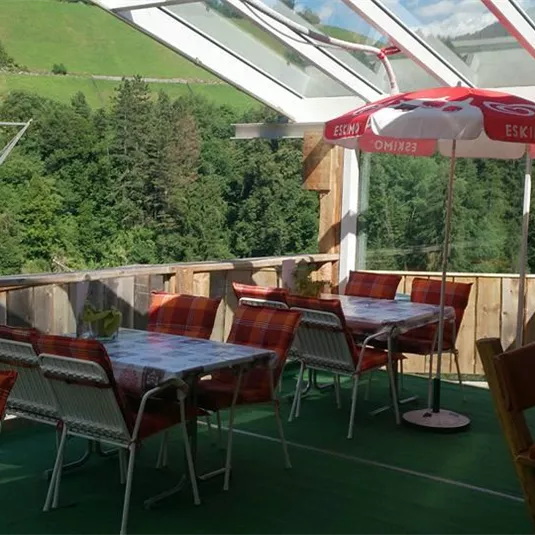 A cozy outdoor area of a café with tables and chairs. In the background, green meadows and trees can be seen.