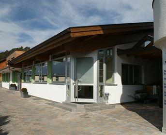 A modern building with large windows and a wooden roof. Surrounded by a beautiful landscape and under a clear sky.