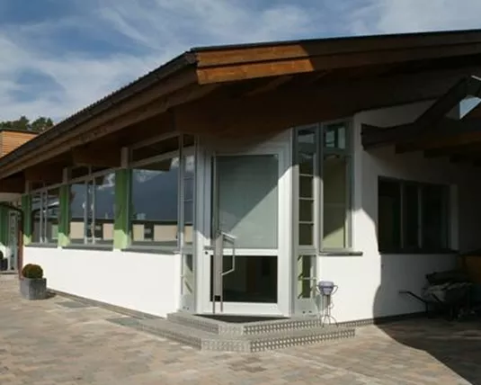 A modern building with a lot of glass and wood. The surroundings are mountainous and the sky is clear.