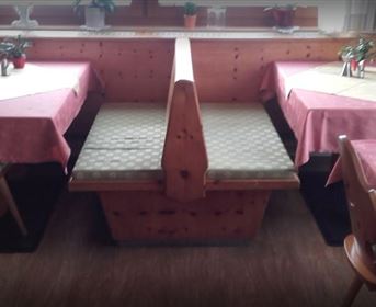 Ein gemütliches Restaurant mit Holztischen und roten Tischdecken. Die Einrichtung ist rustikal und einladend.