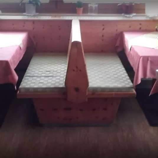 Ein gemütliches Restaurant mit Holztischen und roten Tischdecken. Die Einrichtung ist rustikal und einladend.