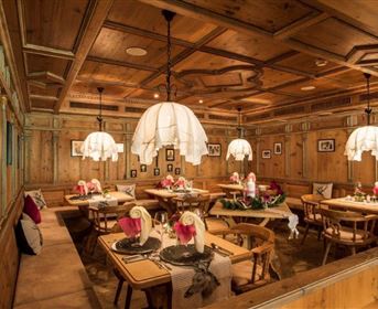 A cozy restaurant with wooden decor and soft lighting. Tables are elegantly set with flowers and stylish tablecloths.