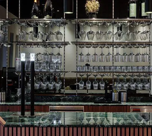 Ein eleganter Barbereich mit einer Glaswand voller Weingläser und Flaschen. Die Theke hat eine moderne, stilvolle Ausstrahlung.