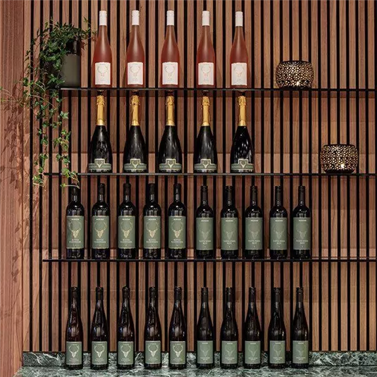 Eine stilvolle Colektion von Weinen und Champagner auf einem eleganten Regal. Daneben eine Pflanze und eine dekorative Laterne.