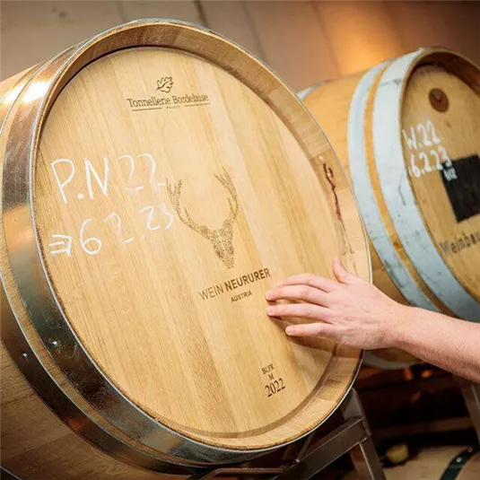 Ein Holzfass mit dem Aufdruck „WEINNEURUR“ und einem Hirschsymbol. Eine Hand berührt die Fassoberfläche.