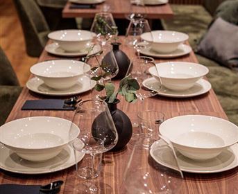 Ein eleganter gedeckter Tisch mit weißen Tellern und Gläsern. In der Mitte steht eine kleine Vase mit einer Pflanze.