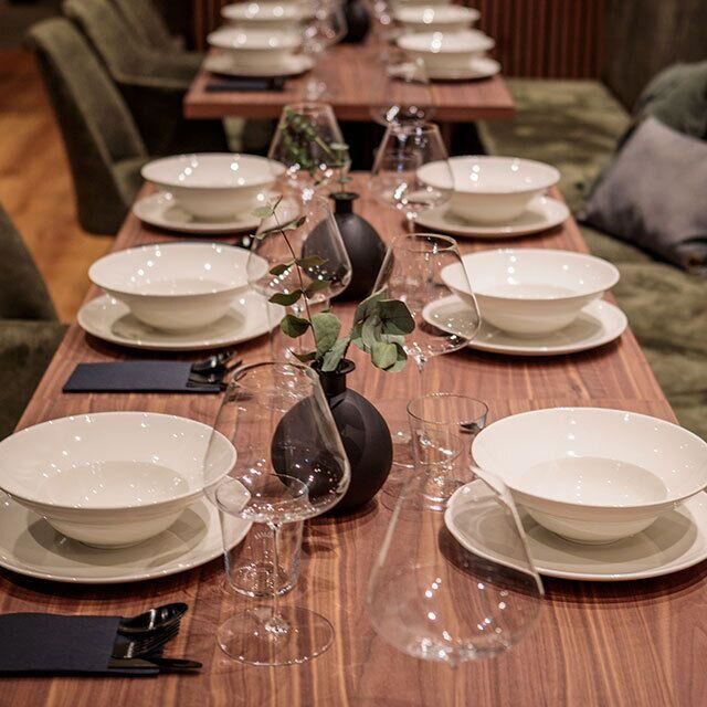 Ein eleganter gedeckter Tisch mit weißen Tellern und Gläsern. In der Mitte steht eine kleine Vase mit einer Pflanze.
