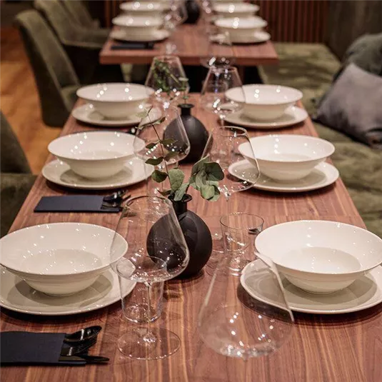 Ein eleganter gedeckter Tisch mit weißen Tellern und Gläsern. In der Mitte steht eine kleine Vase mit einer Pflanze.
