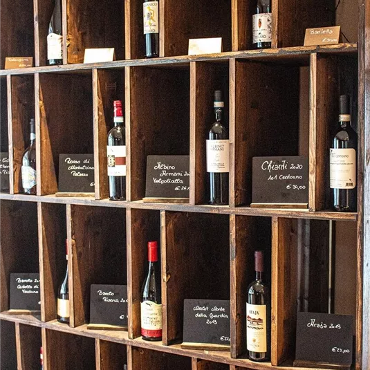 A wooden shelf with multiple compartments, filled with various wine bottles. Each bottle has a price tag indicating the cost.
