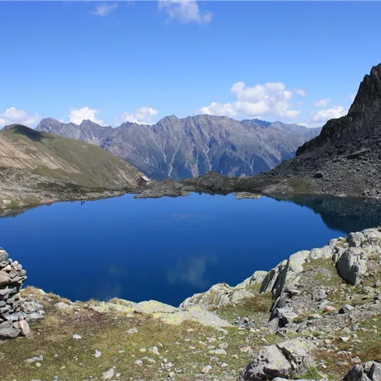 A clear mountain lake surrounded by majestic mountains. The sky is blue and cloudless, creating a tranquil atmosphere.