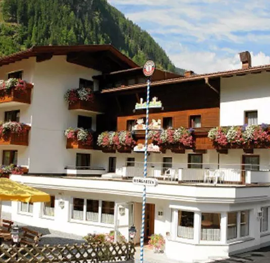 Ein charmantes Hotel mit Balkonblumen in einer malerischen Umgebung. Sonnenschirme und Terrassentische laden zum Verweilen ein.