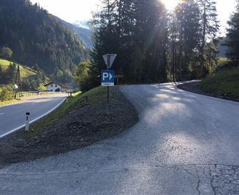 Eine landschaftliche Straße, die sich an einer Parkmöglichkeit teilt. Bäume und Berge umgeben die Szene.