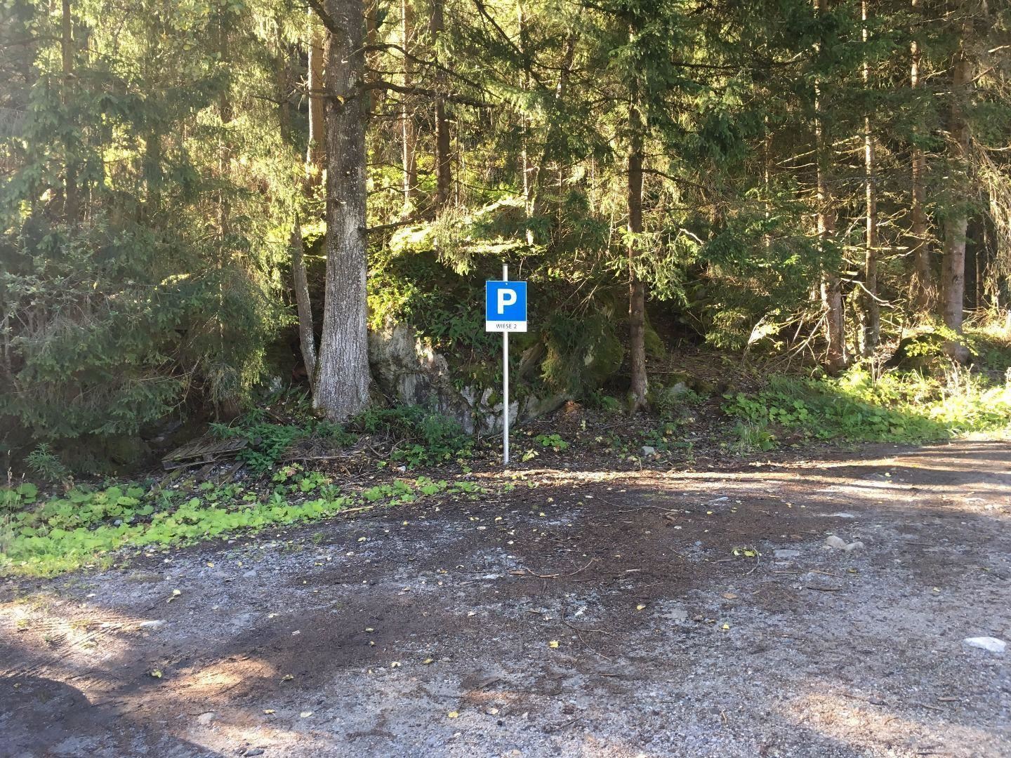 Ein Parkplatzschild steht am Rand eines Waldgebiets. Die Umgebung ist grün und von Bäumen umgeben.