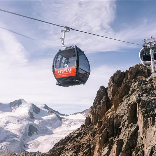 Eine Seilbahn fährt über schneebedeckte Berge. Der Himmel ist klar und die Aussicht ist beeindruckend.