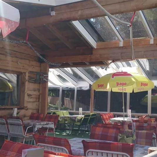 A cozy interior with wooden paneling and large windows. There are colorful sun umbrellas and tables with chairs that invite you to linger.