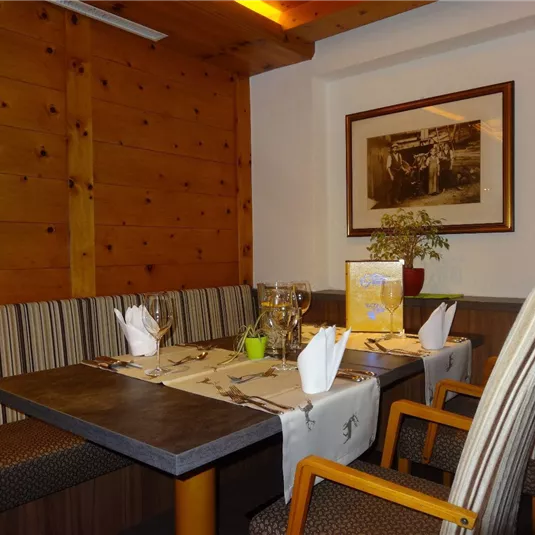 Ein gemütlicher Restaurantbereich mit Holzwänden und einer eleganten Tischdekoration. Die Tische sind mit Gläsern und Servietten sorgfältig gedeckt.