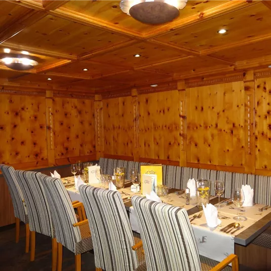 Ein gemütlicher Restaurantbereich mit Holzwänden und einer langen Tafel. Die Stühle sind gestreift und der Raum ist gut beleuchtet.