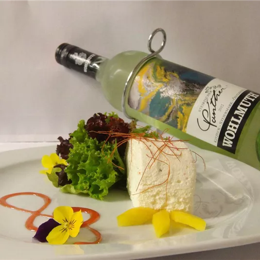 Ein eleganter Teller mit frischem Salat, einer Käseportion und essbaren Blüten. Daneben steht eine Flasche Wein, die das Gericht ergänzt.