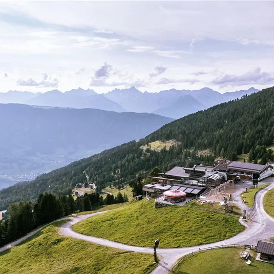 A picturesque mountain landscape with gentle hills and green meadows. In the background, impressive mountains and a cloudy sky are visible.