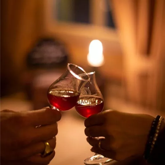 Zwei Gläser werden zum Anstoßen gehalten. Im Hintergrund ist ein warmes, gemütliches Licht zu sehen.
