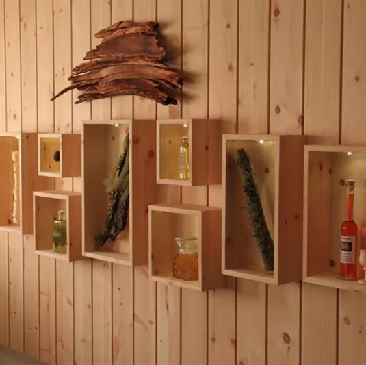 Eine dekorative Wand mit hellen Holzregalen, die verschiedene Flaschen und Pflanzen zeigen. Die sanfte Beleuchtung hebt die Präsentation hervor.