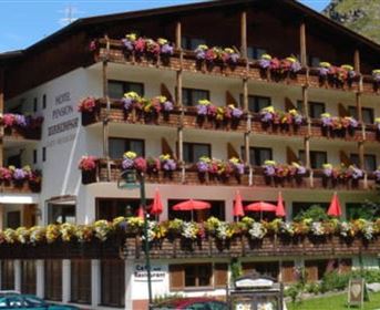 Ein charmantes Hotel mit sichtbaren Balkonen, die mit bunten Blumen geschmückt sind. Der Himmel ist klar und die Umgebung ist grün.