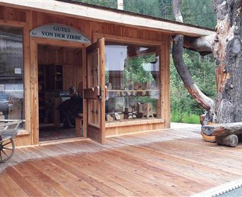 Ein Holzladen mit großen Fenstern und einer einladenden Tür. Draußen steht ein Wagen und im Hintergrund sind Bäume zu sehen.