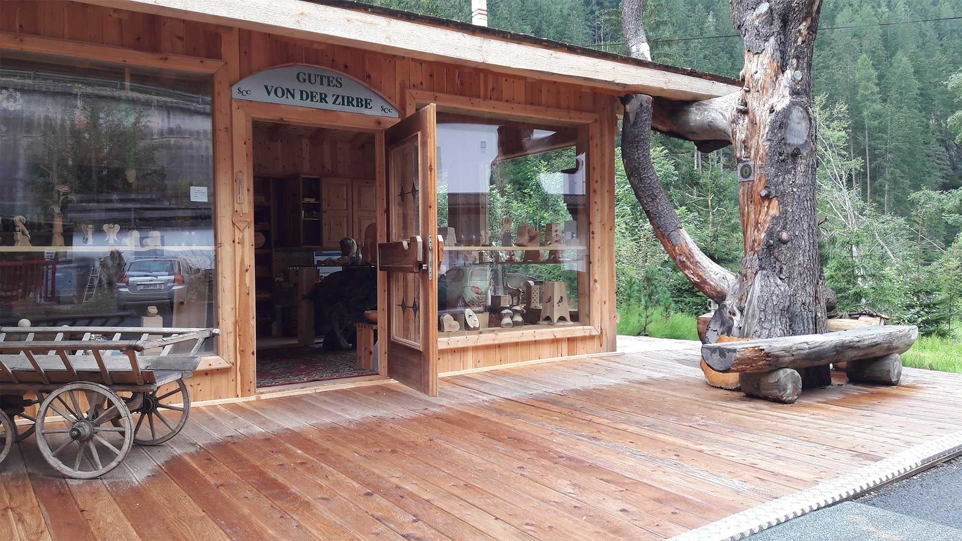 Ein Holzladen mit großen Fenstern und einer einladenden Tür. Draußen steht ein Wagen und im Hintergrund sind Bäume zu sehen.