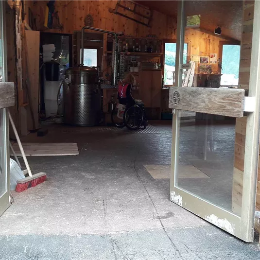 Ein Eingang zu einem Holzgebäude mit offenen Türen. Im Inneren sind Werkzeuge und verschiedene Gegenstände zu sehen.