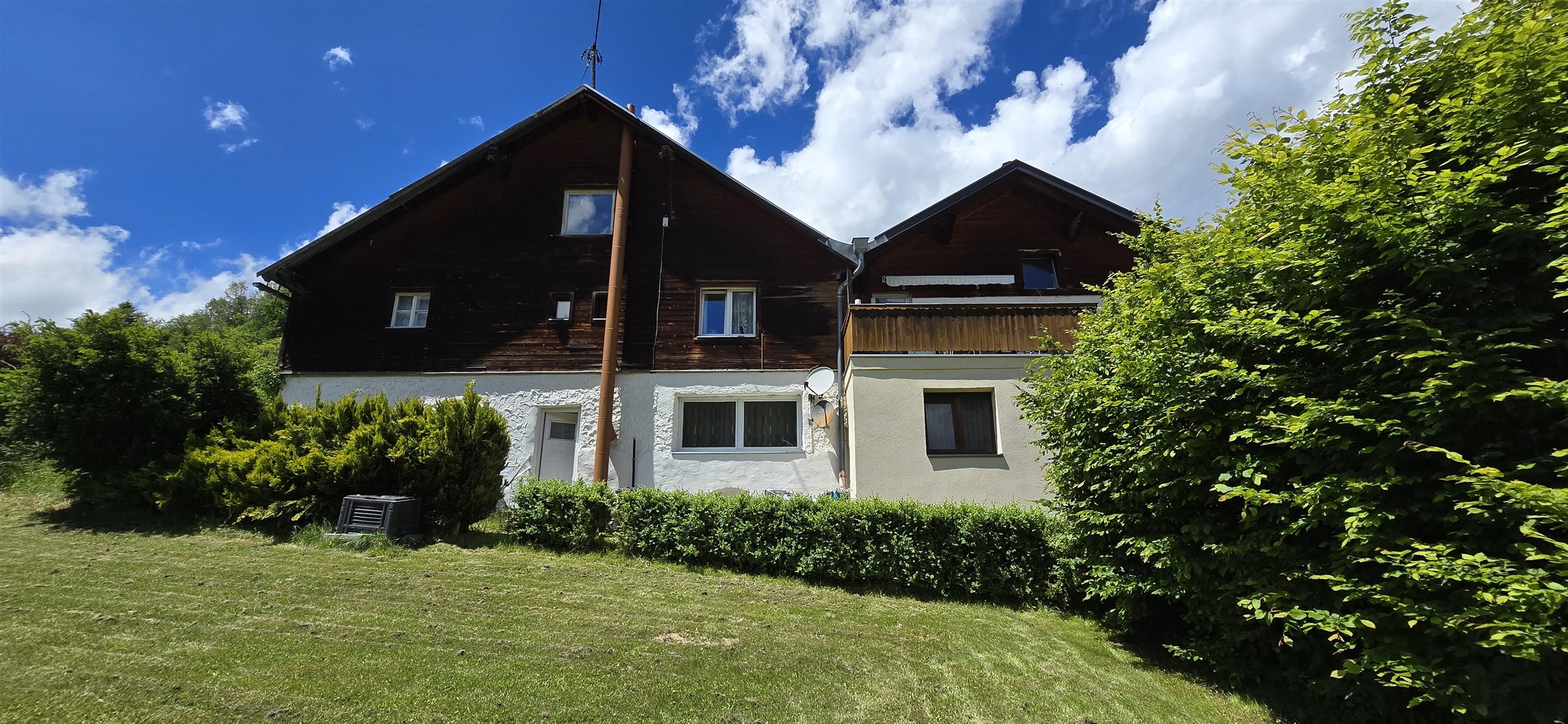 A charming house with a wood and stucco facade, surrounded by green grass and bushes. The sky is blue with a few clouds.