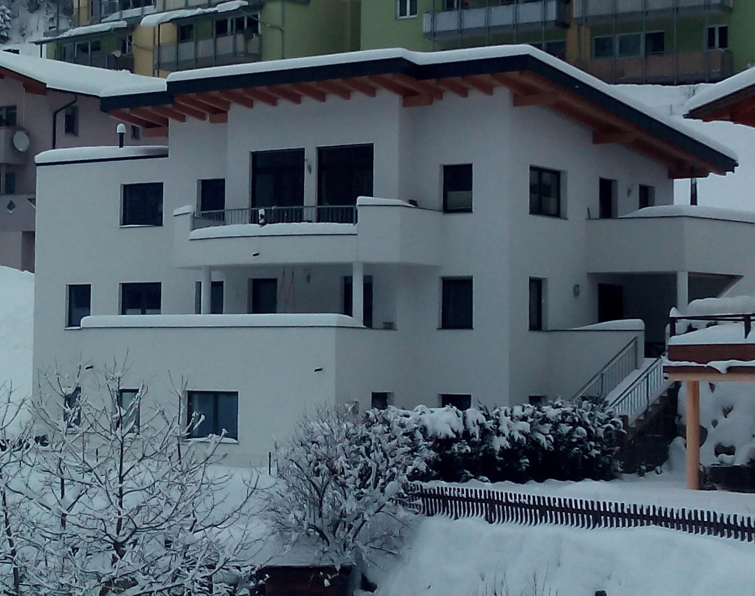A modern, white house in the snow. The surroundings are wintry with snow-covered trees and a tranquil atmosphere.