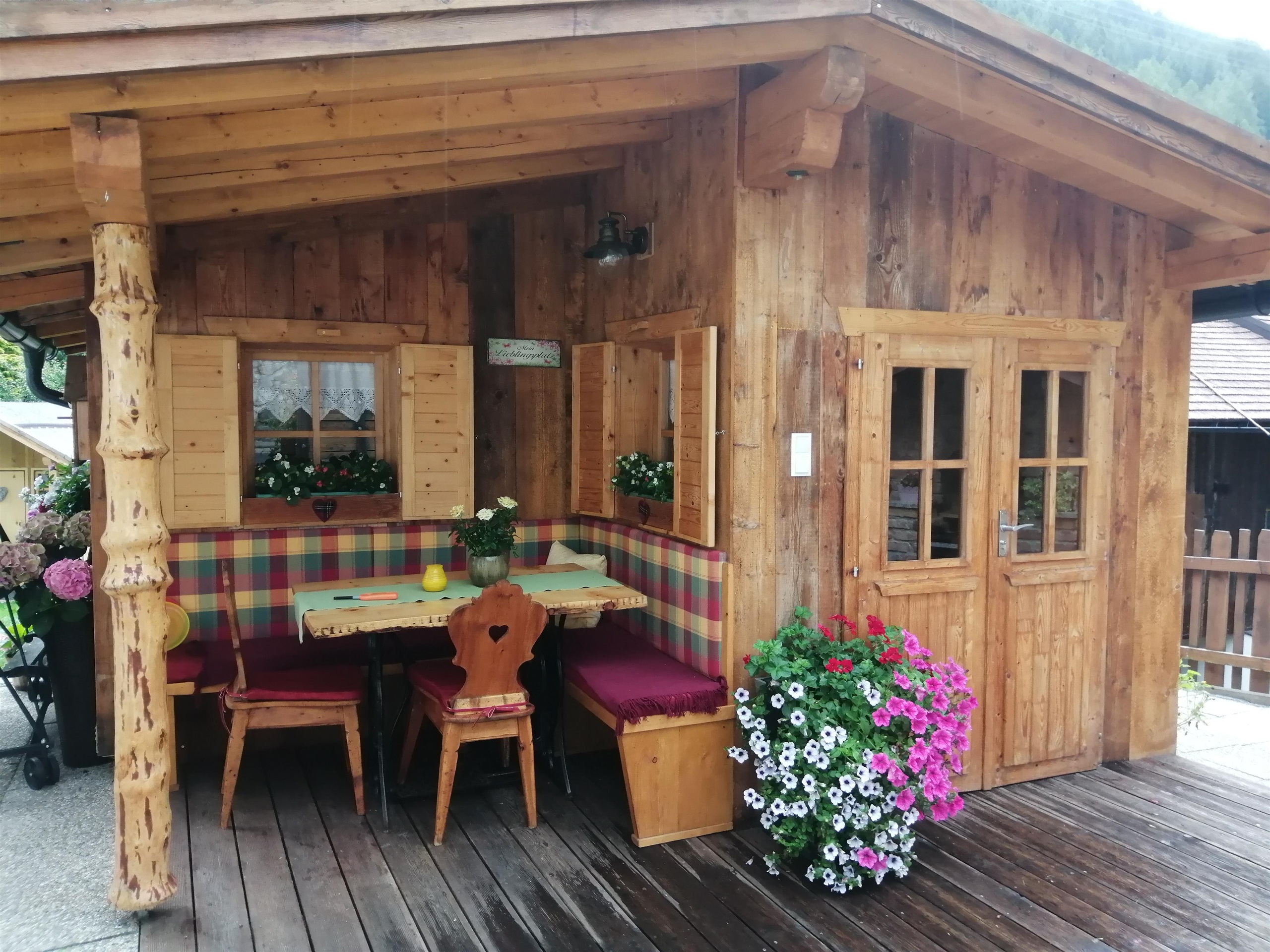 Eine gemütliche Holzhütte mit einem einladenden Essbereich und bunten Blumen. Der Außenbereich ist mit Holz und sichtbaren Pflanzen geschmückt.