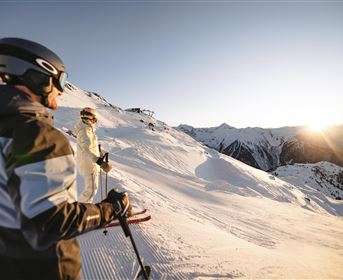 Two skiers are skiing on a snow-covered slope. The sun is shining and the sky is clear.