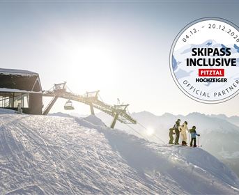A group of skiers stands on a snowy summit overlooking the mountains. In the background, a cable car can be seen leading to the valley station.