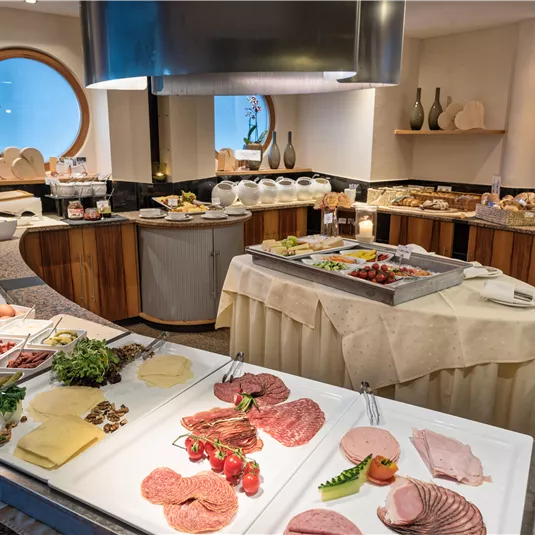Ein reichhaltiges Frühstücksbuffet mit einer Auswahl an Wurst, Käse, frischem Gemüse und Brot. Das Ambiente ist modern und einladend.
