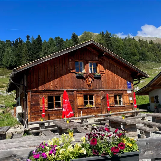 A cozy wooden mountain hut surrounded by green forests. Outdoor tables invite you to linger.